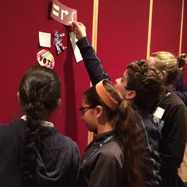 Color photo of a small group of teens places pictures on a velcro board.