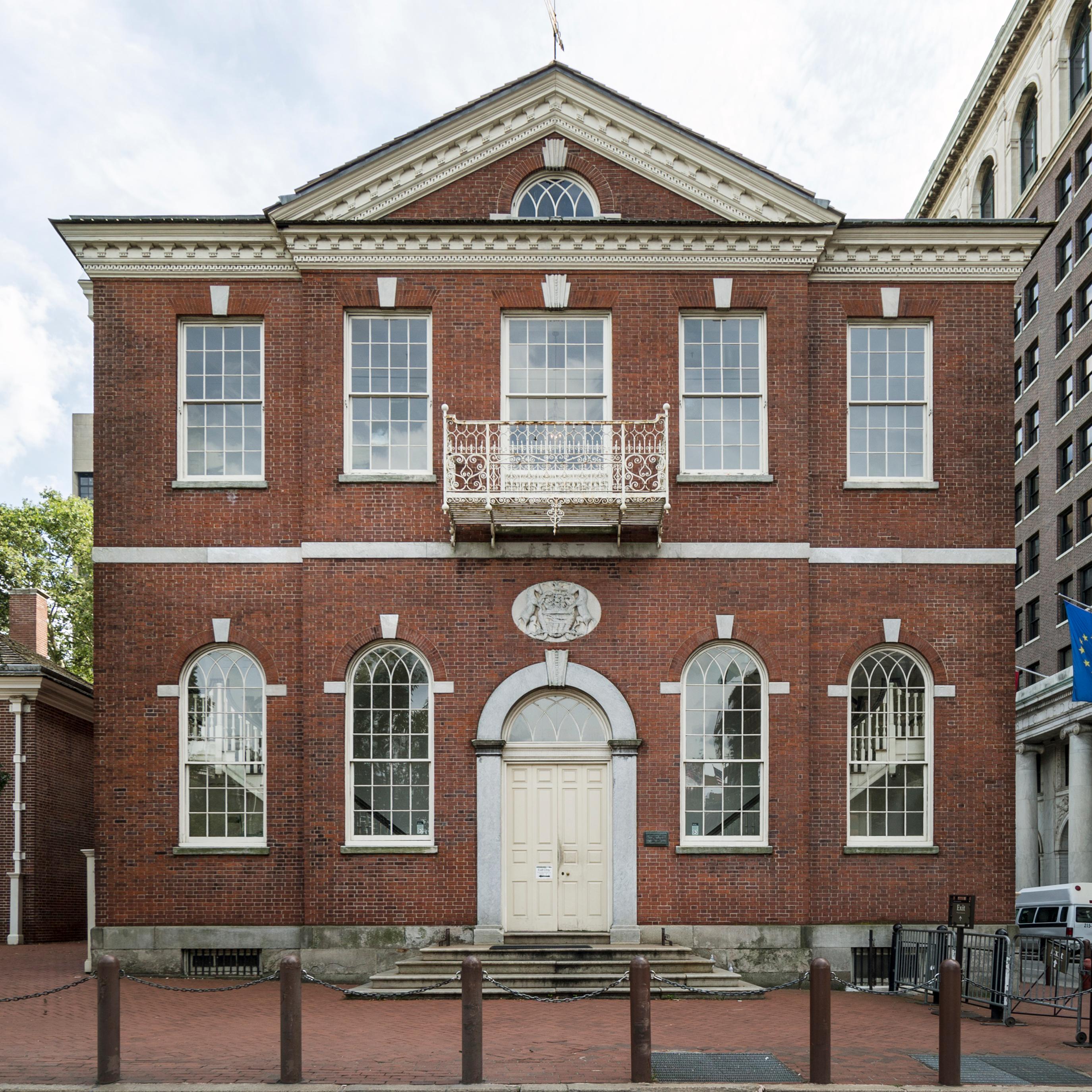 Color photo of the exterior of a two story red brick building with center door and pediment.
