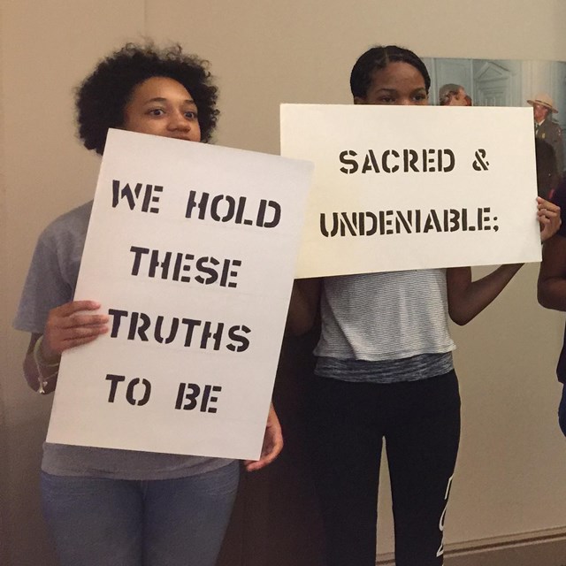 Color photo of teens holding up cards bearing phrases from the Declaration of Independence.