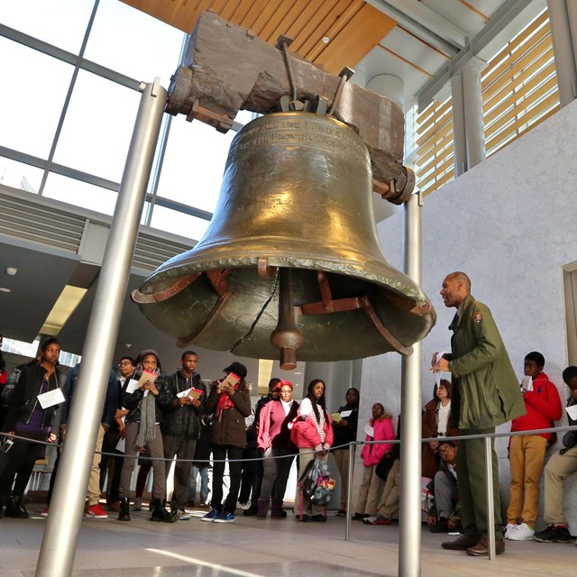 Color photo of teens looking at a large bell