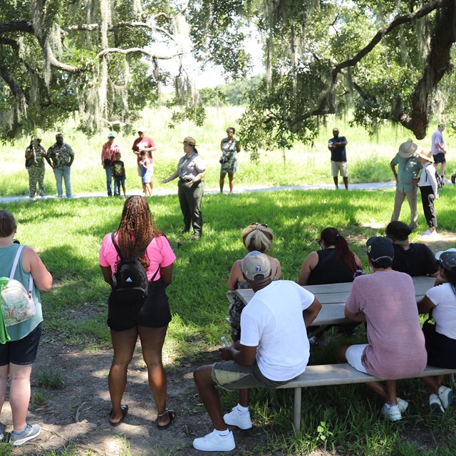 A park ranger gives a talk surrounded by a crowd of numerous visitors. 