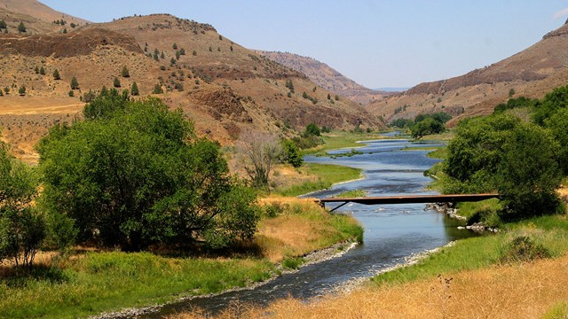 A river winds through a grassy valley with some trees on the banks.