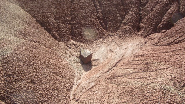 A small crevice in red, cracked soil with a red rock in the bottom of the crevice.