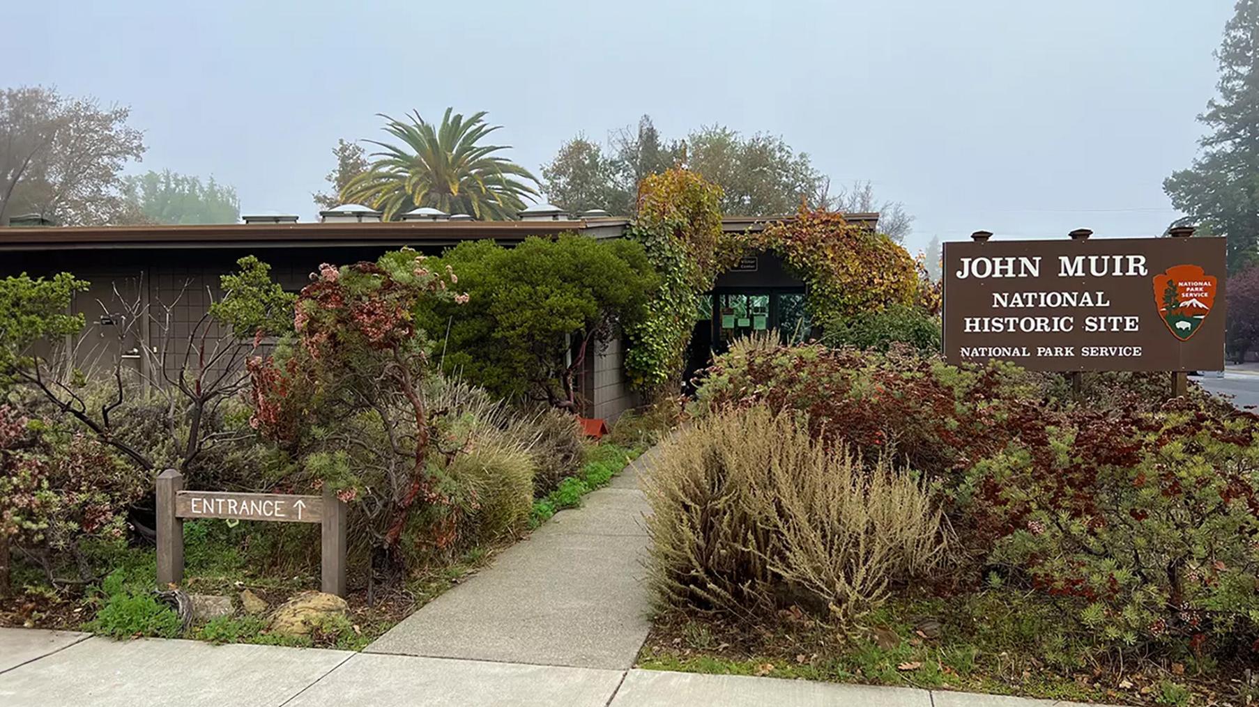 John Muir National Historic Site entrance with a pathway, native plants, and a park sign.