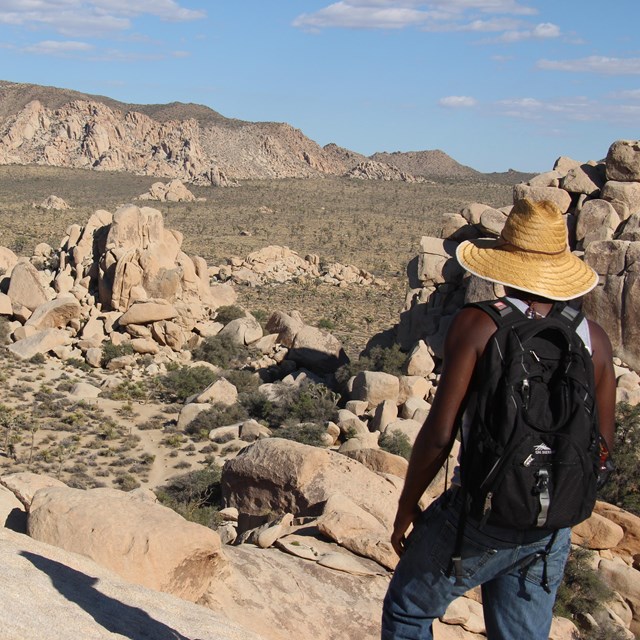 a hiker standing high on a rock outcrop looks over a desert valley