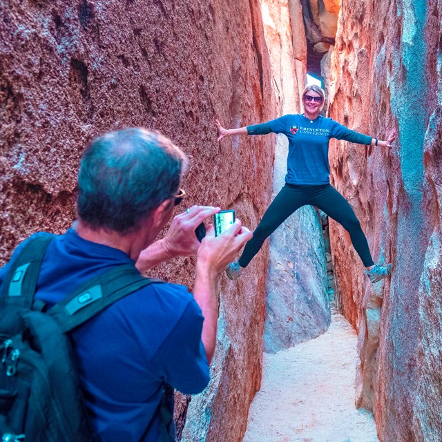 A woman poses for a photo and braces against the sides of a slot canyon.