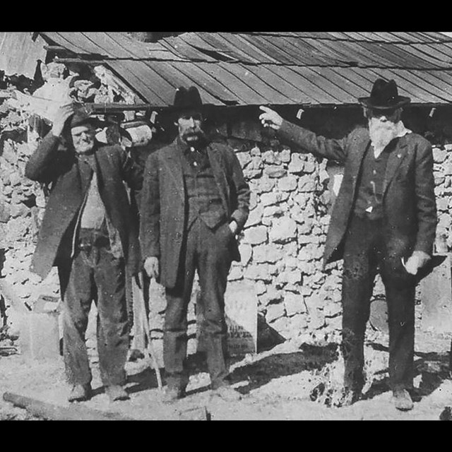 a black and white photo of three men in front of a cabin