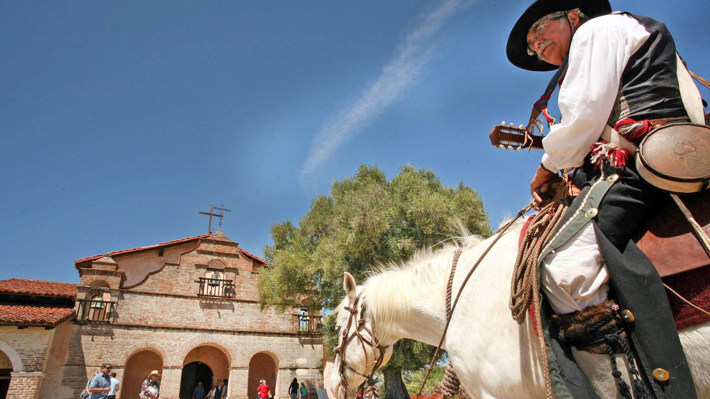 A rider sits mounted on a horse outside Mission San Antonio 