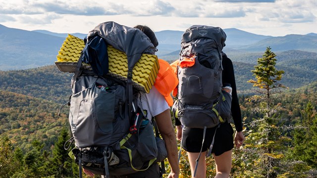 Two backpackers on the summit of Lunksoos Mountain with other mountains in distance.