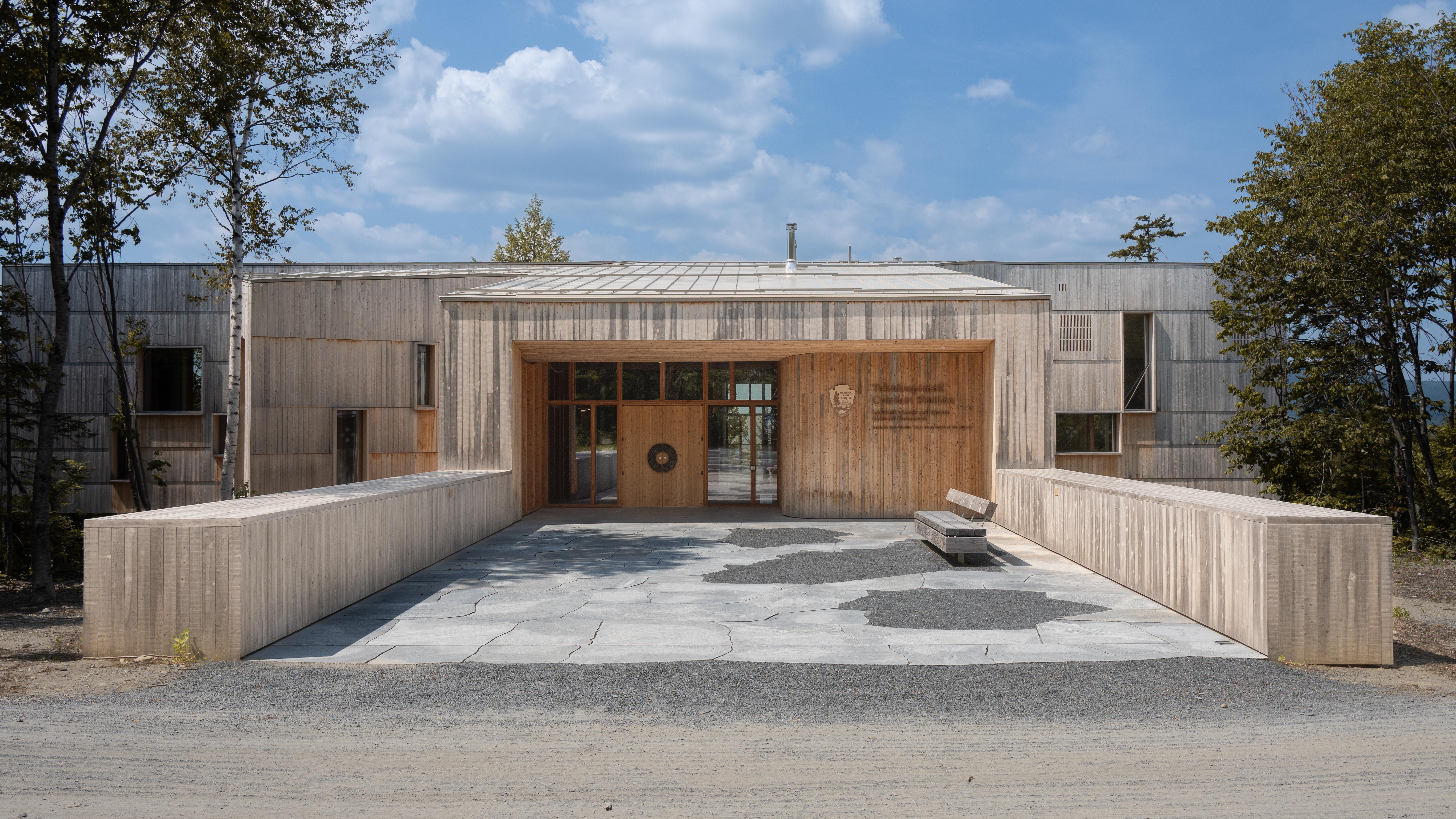 A large wooden building sits in the photo against a blue sky with clouds. A walkway extends outward.