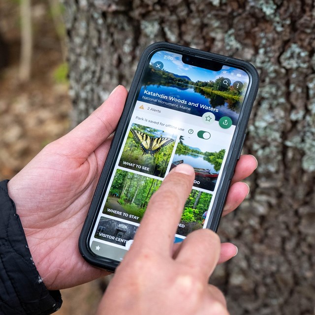 A close up photo of a person navigating the Katahdin Woods and Waters NM Page on the NPS App.