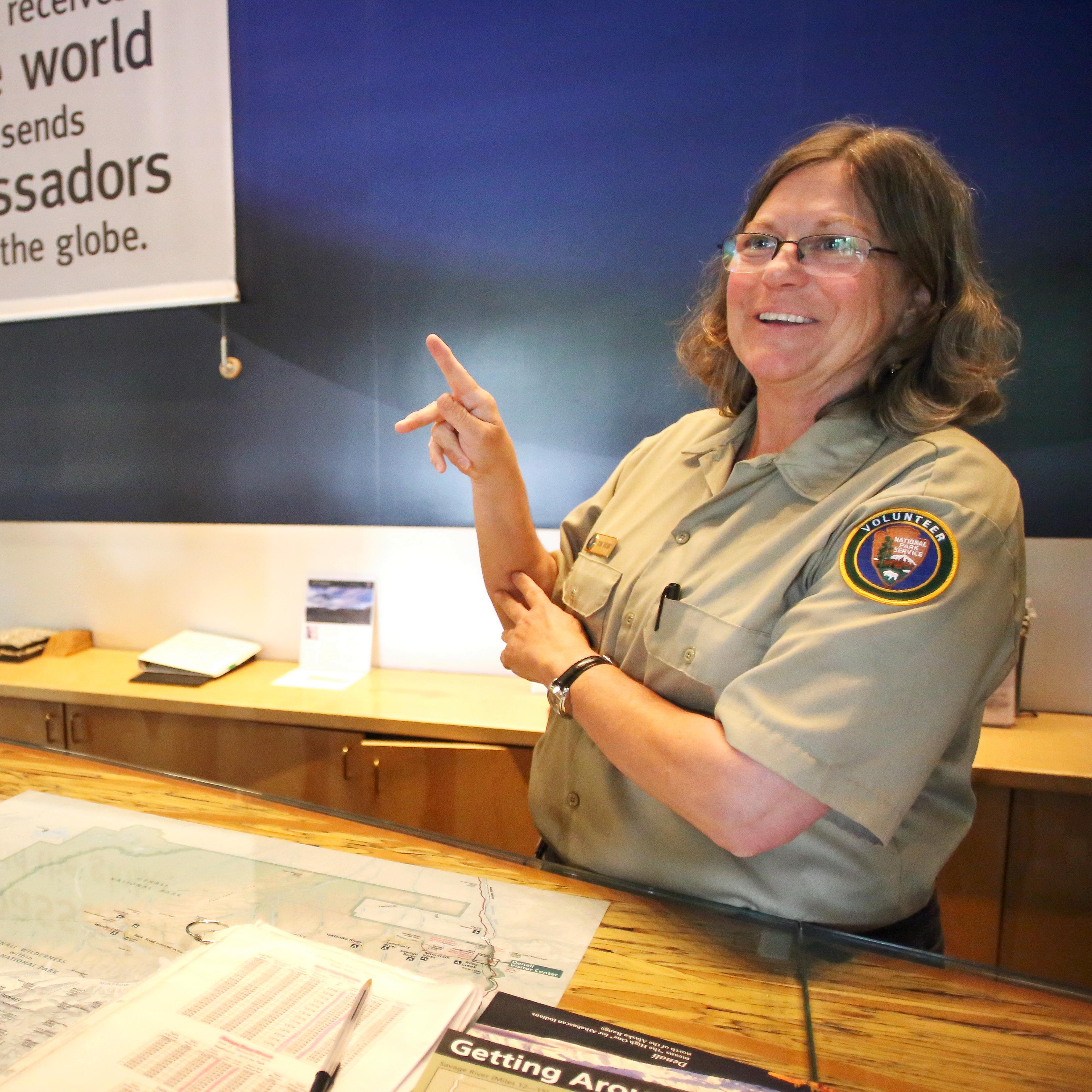A person in an NPS volunteer uniform makes the letter K in American Sign Language with their hands.