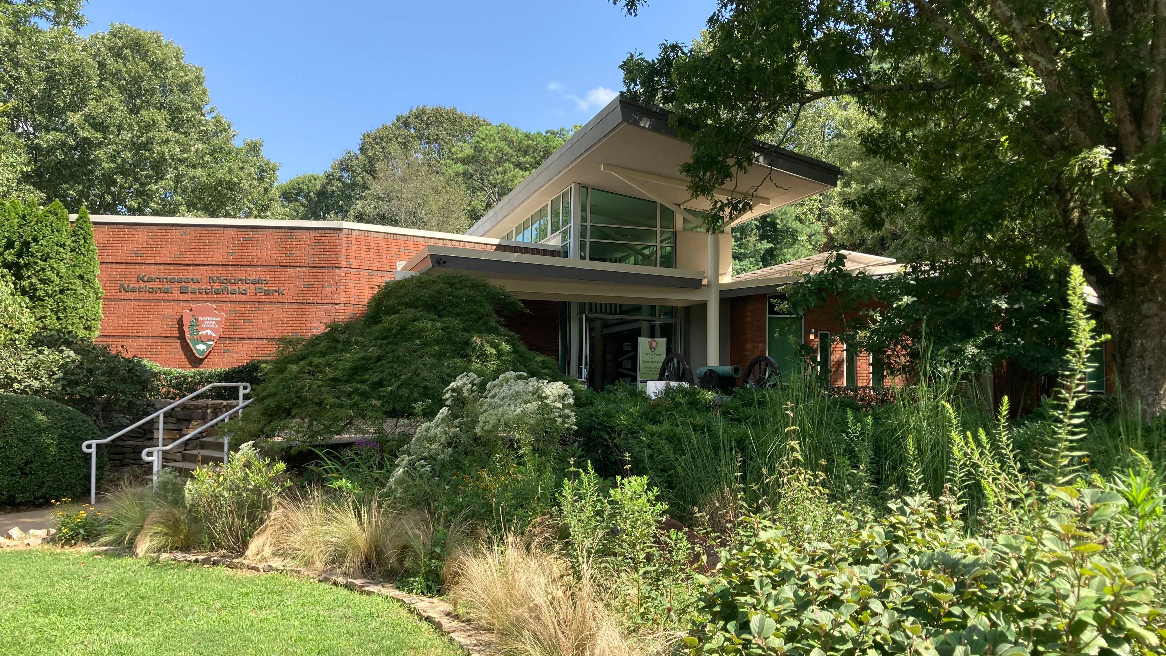 Image of brick visitor center with green vegetation in front.