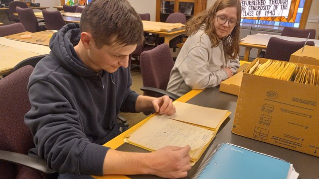 A young man and woman sitting at a table looking at historic documents.