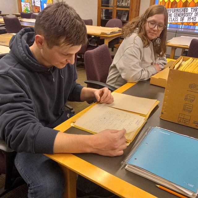 A young man and woman sitting at a table looking at historic documents.