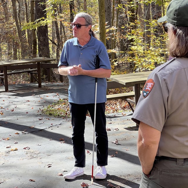 A man stands with a white cane and sunglasses.