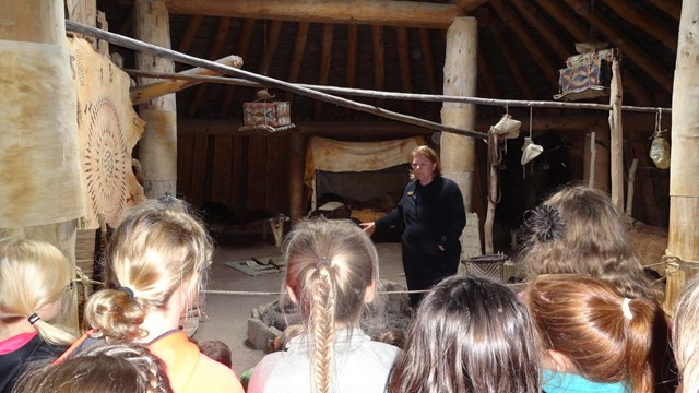 6 students listen to a female ranger's presentation inside an earthlodge.
