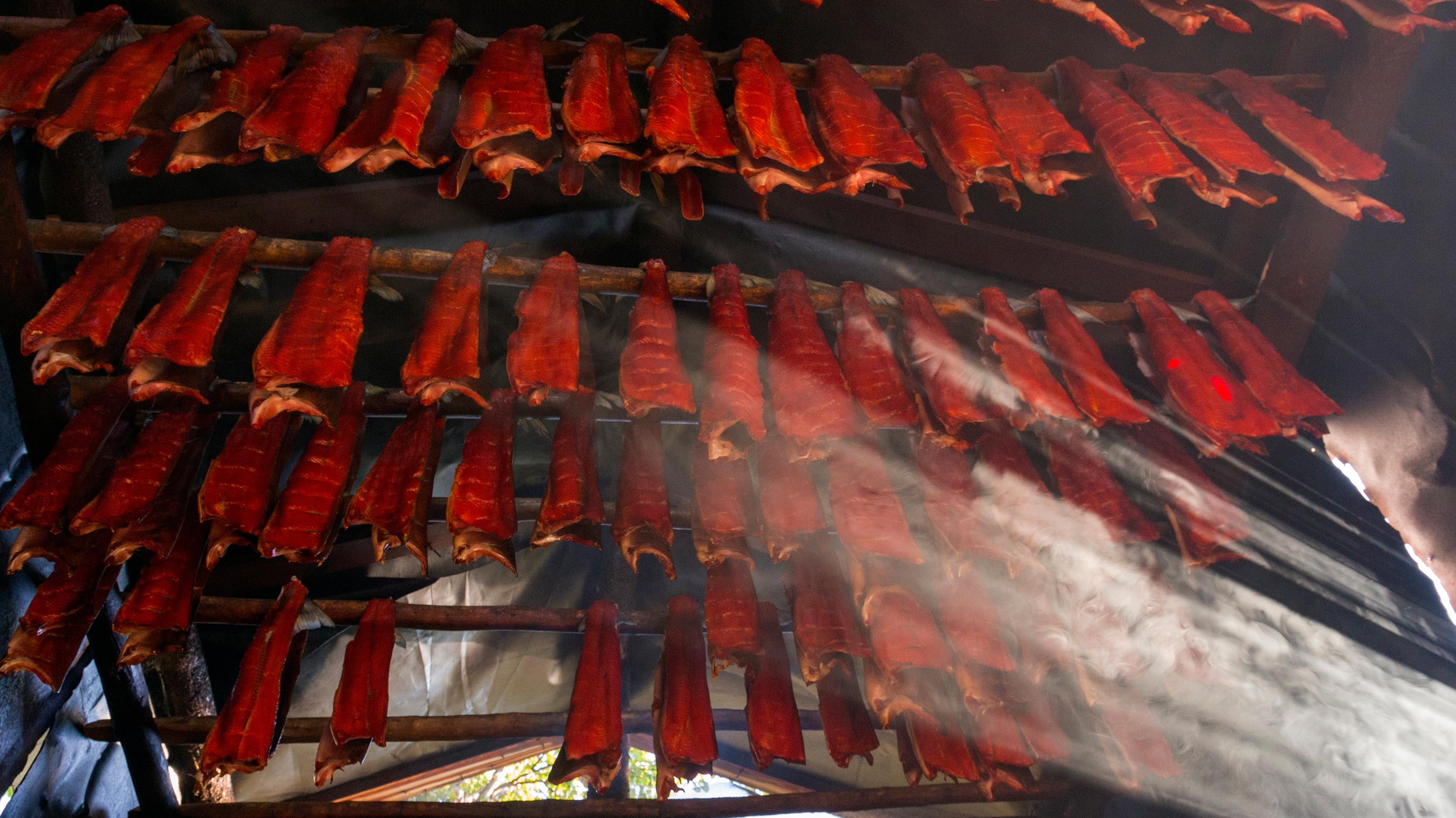 Rows of drying salmon fillets hang from wooden rods in smoke house.