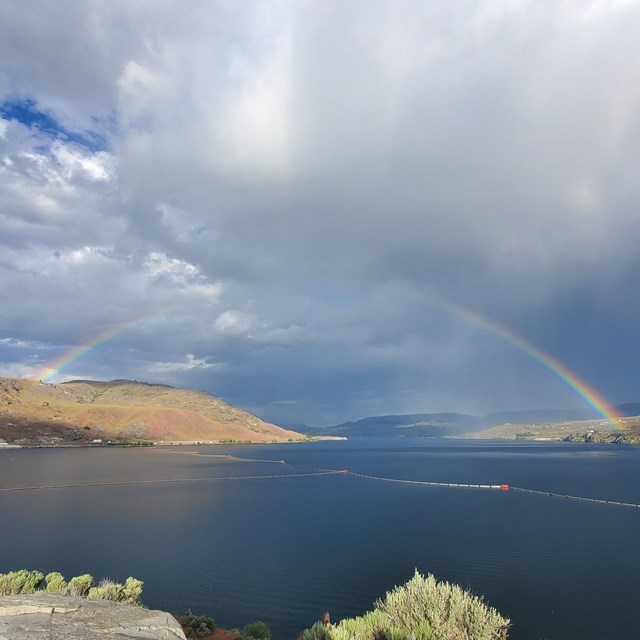 A rainbow overarching a dark blue lake.