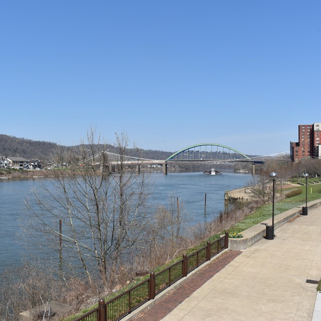 paved walking path near river with bridge in view