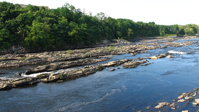 The Merrimack River is flowing from the front left to mid right of the frame, with rock outcroppings