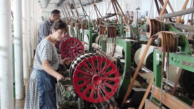 A weaver stands a row of power looms