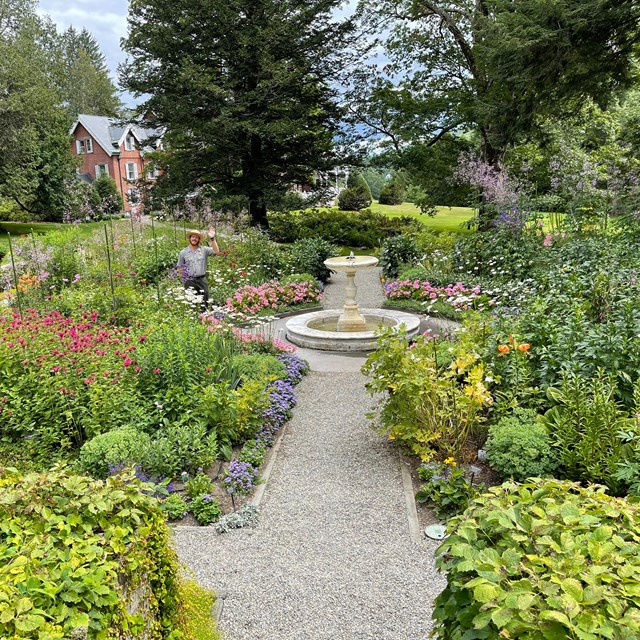 park ranger waves at camera from formal four square garden