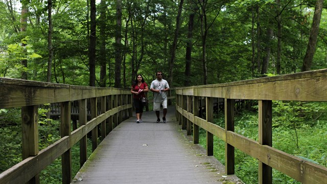 Two people walking on a wooden boardwalk. 