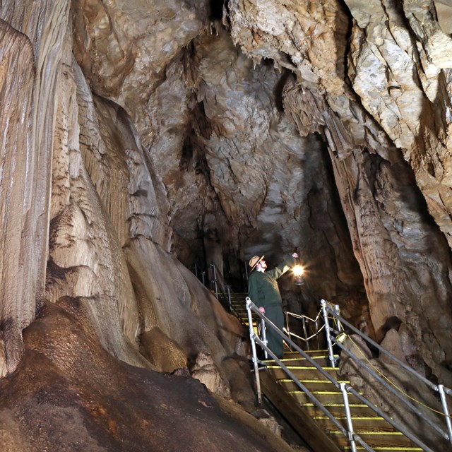 A caver holding a lantern admires the cave formations.