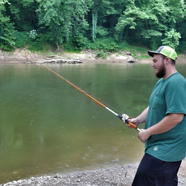 A young man fishing along a river