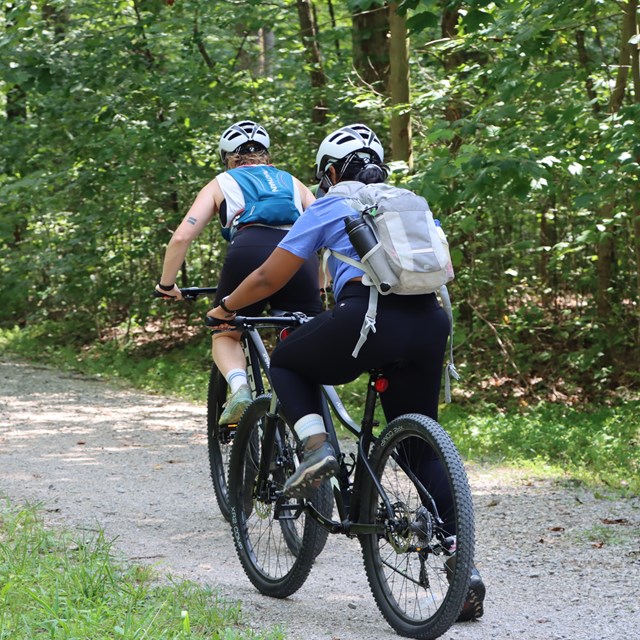 Two people ride bikes on a gravel path.