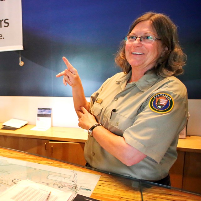 A person in an NPS volunteer uniform makes the letter K in American Sign Language with their hands.