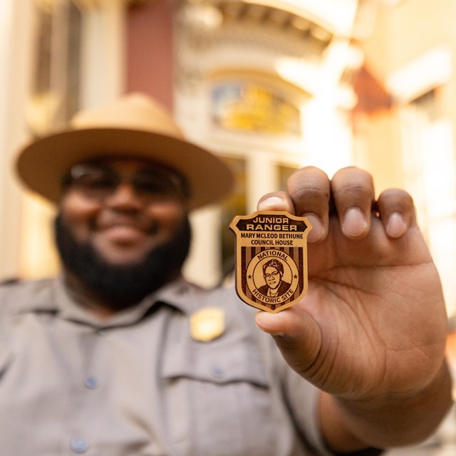 A male ranger in uniform holds a Council House Junior Ranger Badge