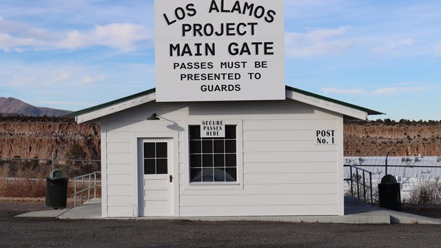 A white building with a big sign that reads, "Los Alamos Project Main Gate"