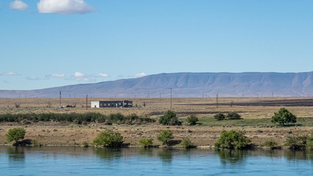 A lone building on a riverbank with mountains in the background.