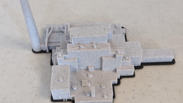 Grey model of a blocky industrial building with a tall smokestack set on a light gray table.