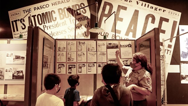 A woman in a uniform is pointing to pieces of paper displayed in a cubicle to three children. On the