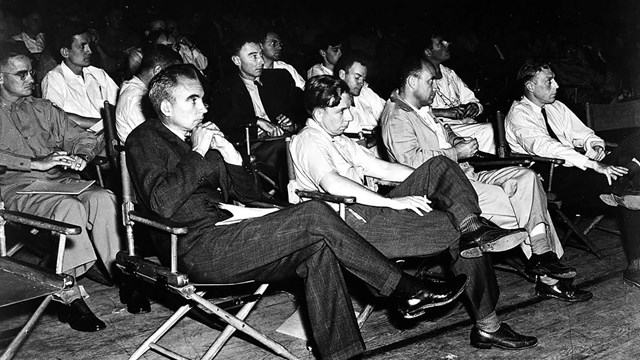 About 15 people sitting in folding chairs in rows looking off to the right.