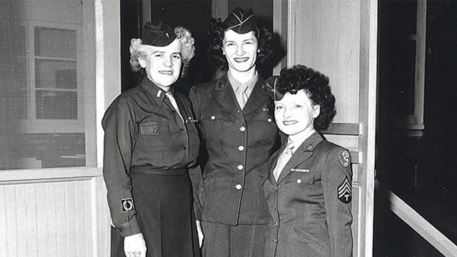 A black and white image of three woman in uniforms standing side-by-side. 