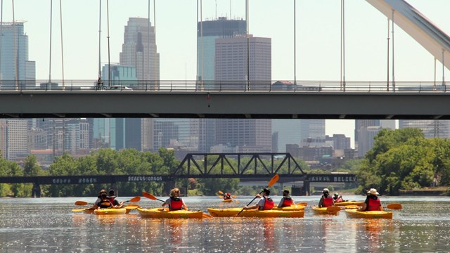 Group of kayakers paddle under Lowry Avenue Bridge.