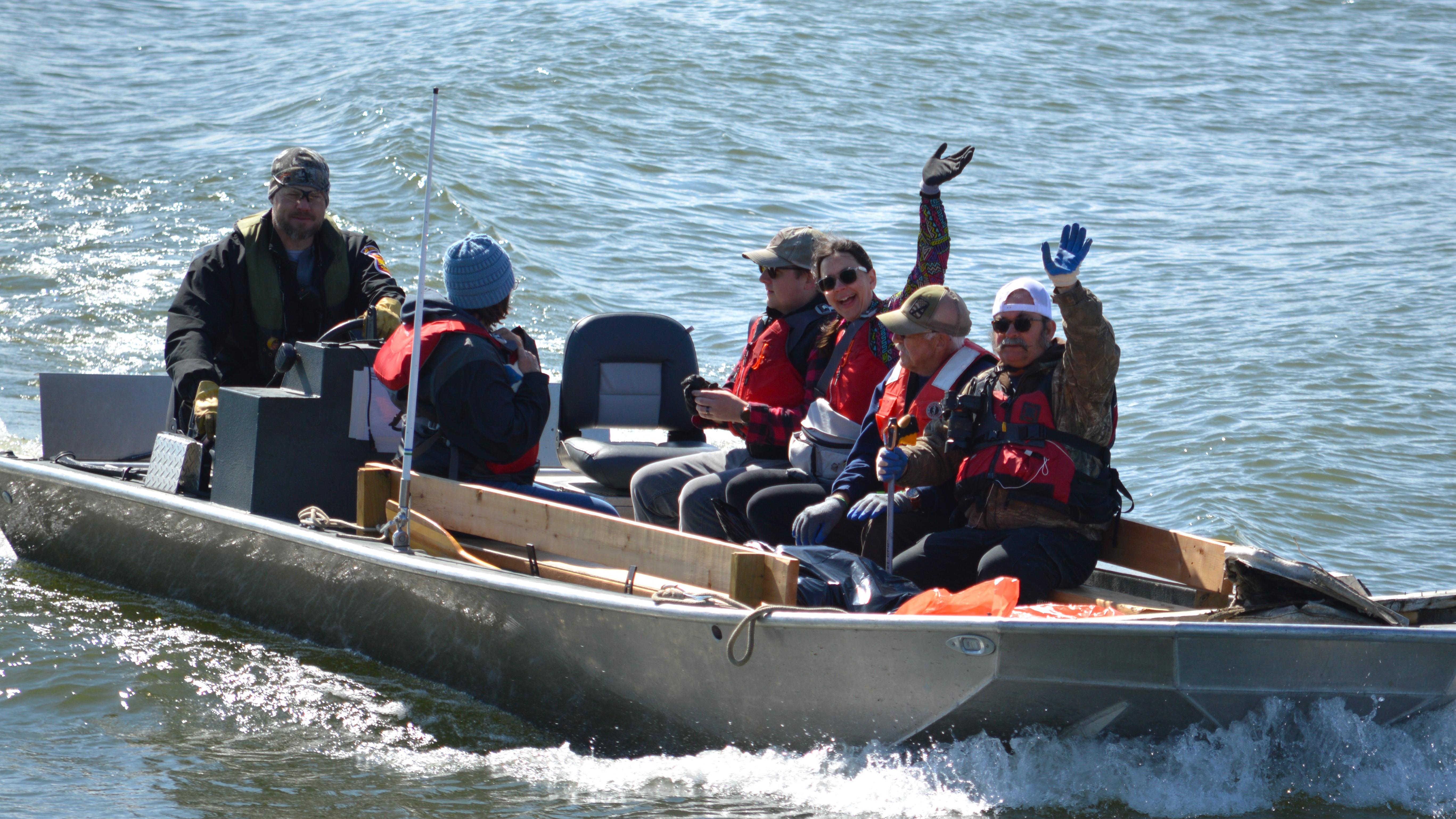 A group of people ride in a motorized boat. Two people are waving.