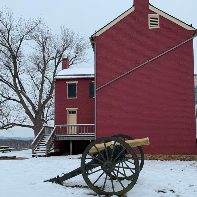 A Civil War-era cannon sits in front of a red brick farmhouse.