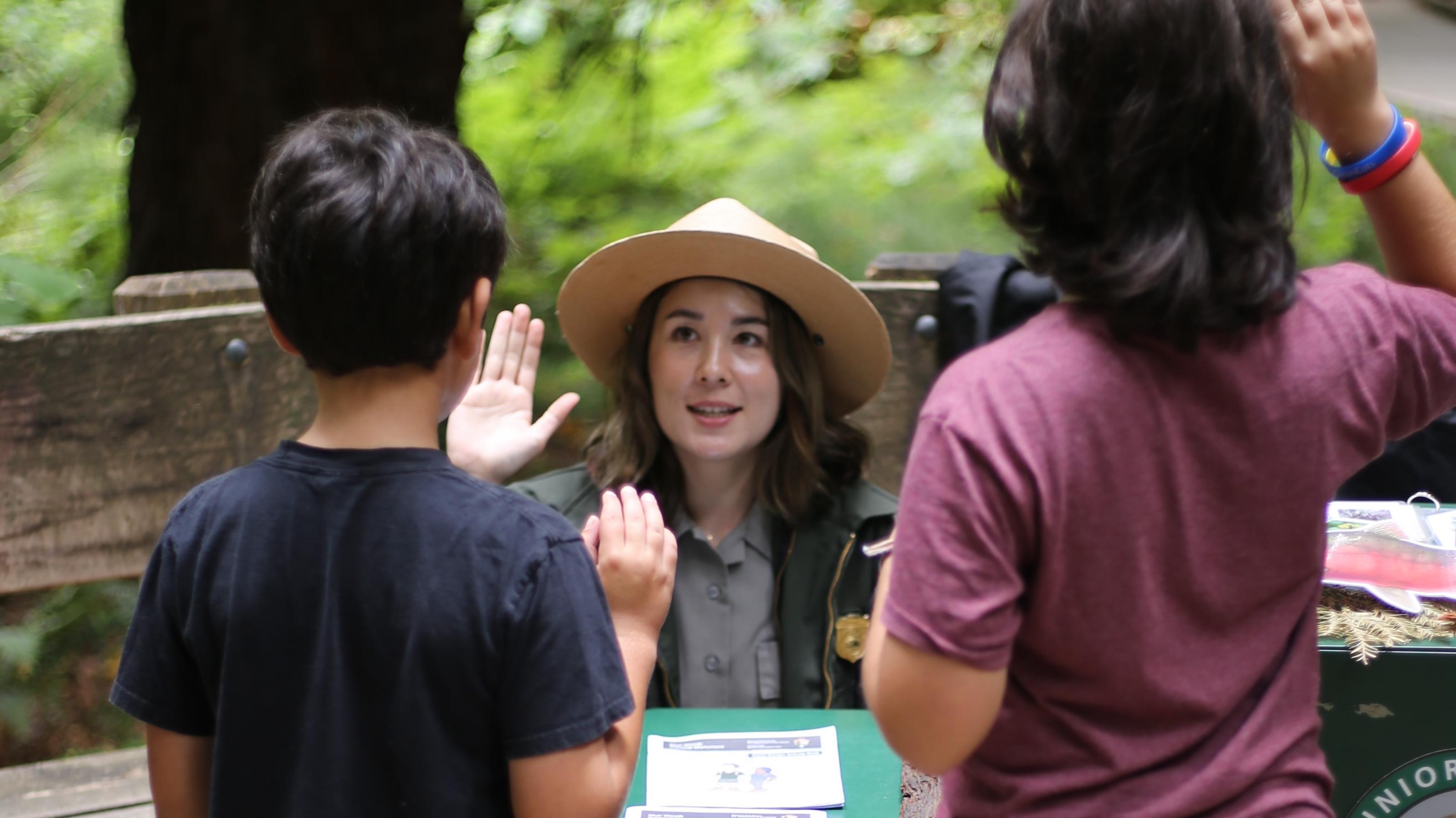 a uniformed ranger raises her right hand as she swears in two young junior rangers