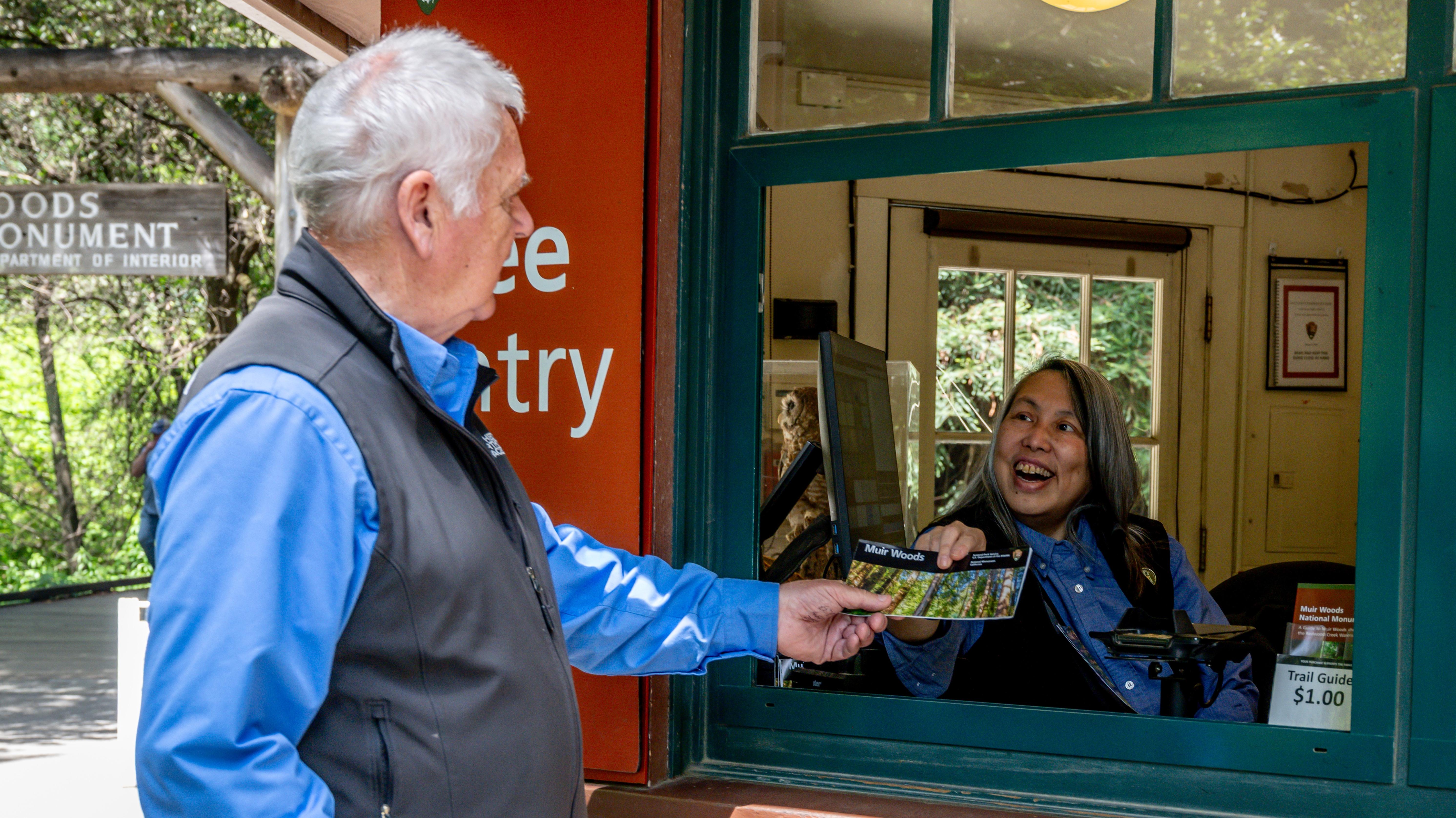 a fee collector in a booth passes a brochure to a visitor