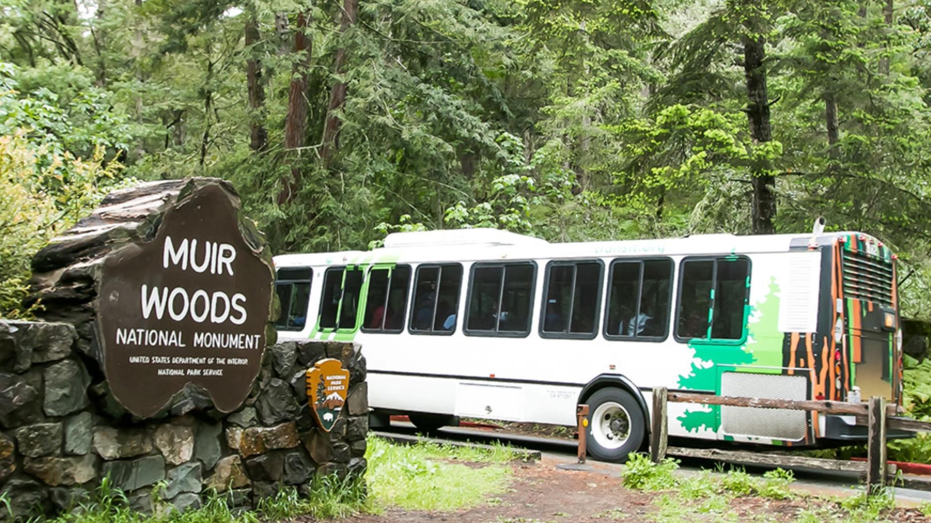 a bus drives past a sign that reads Muir Woods National Monument