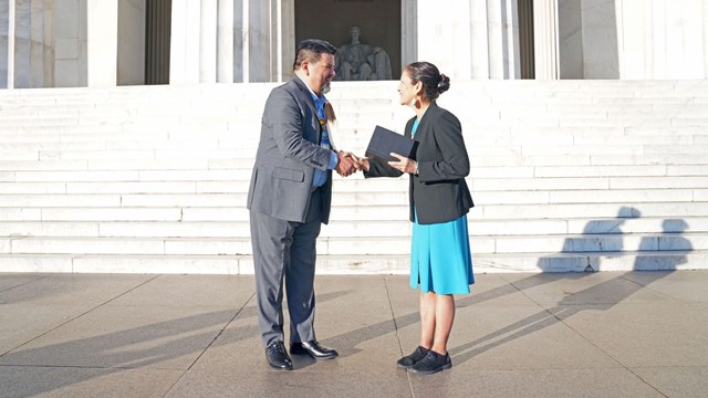 A man and a womand shaking hands on the steps of the Lincoln Memorial