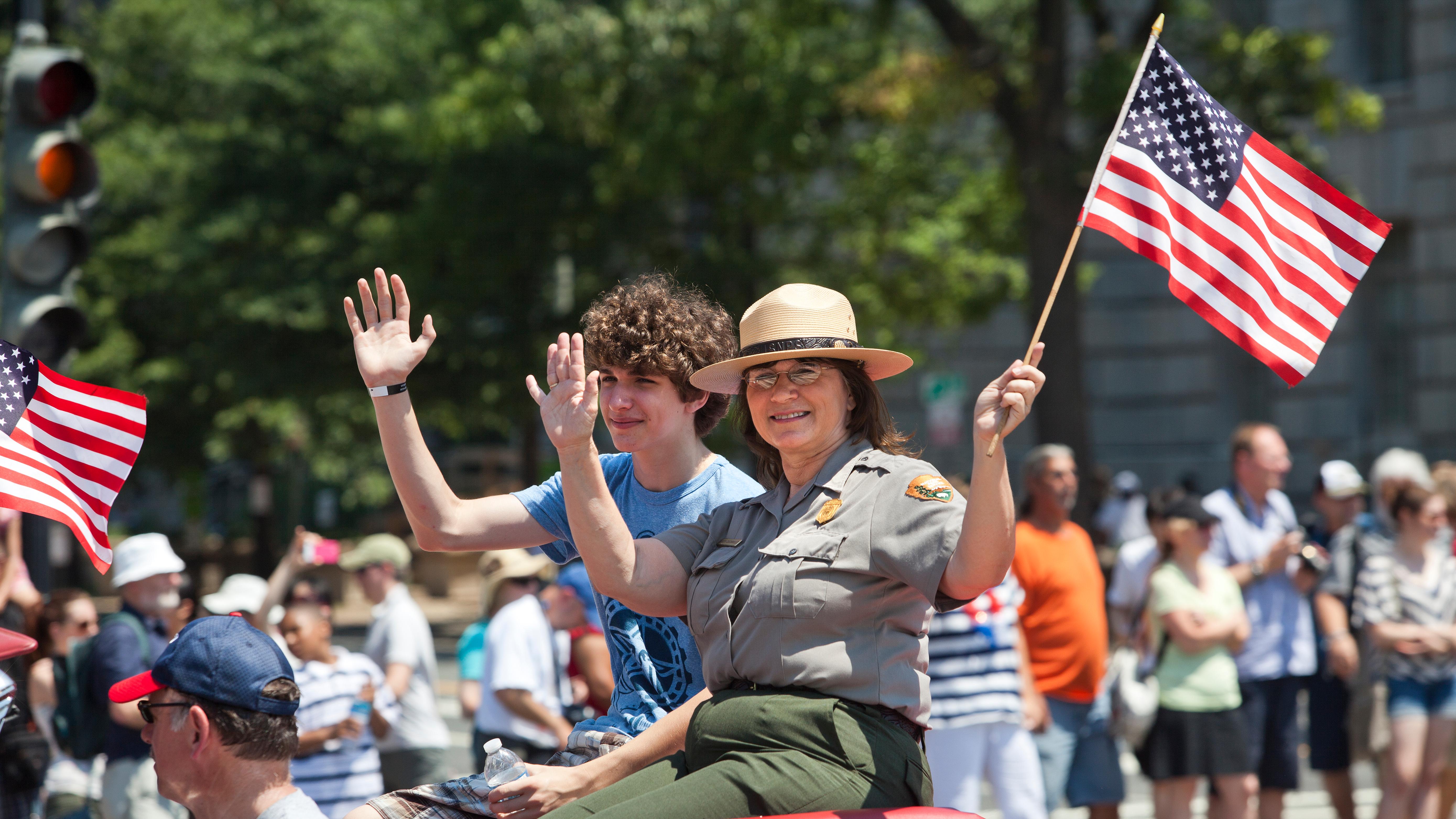 A Park Ranger waves an American Flag from a parade car in the Independence Day Parade.