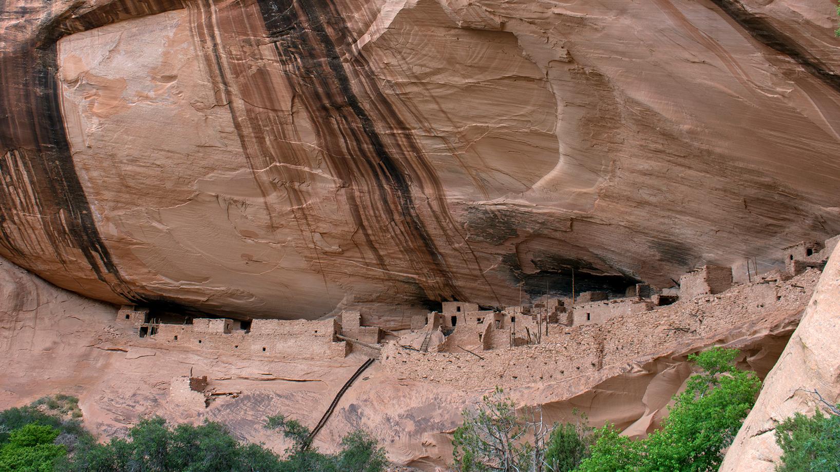 Houses made of sandstone, mud mortar, and wood are sheltered in a cliff alcove. 