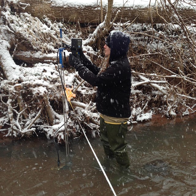 Field technician stands in a stream with water quality monitoring equipment.
