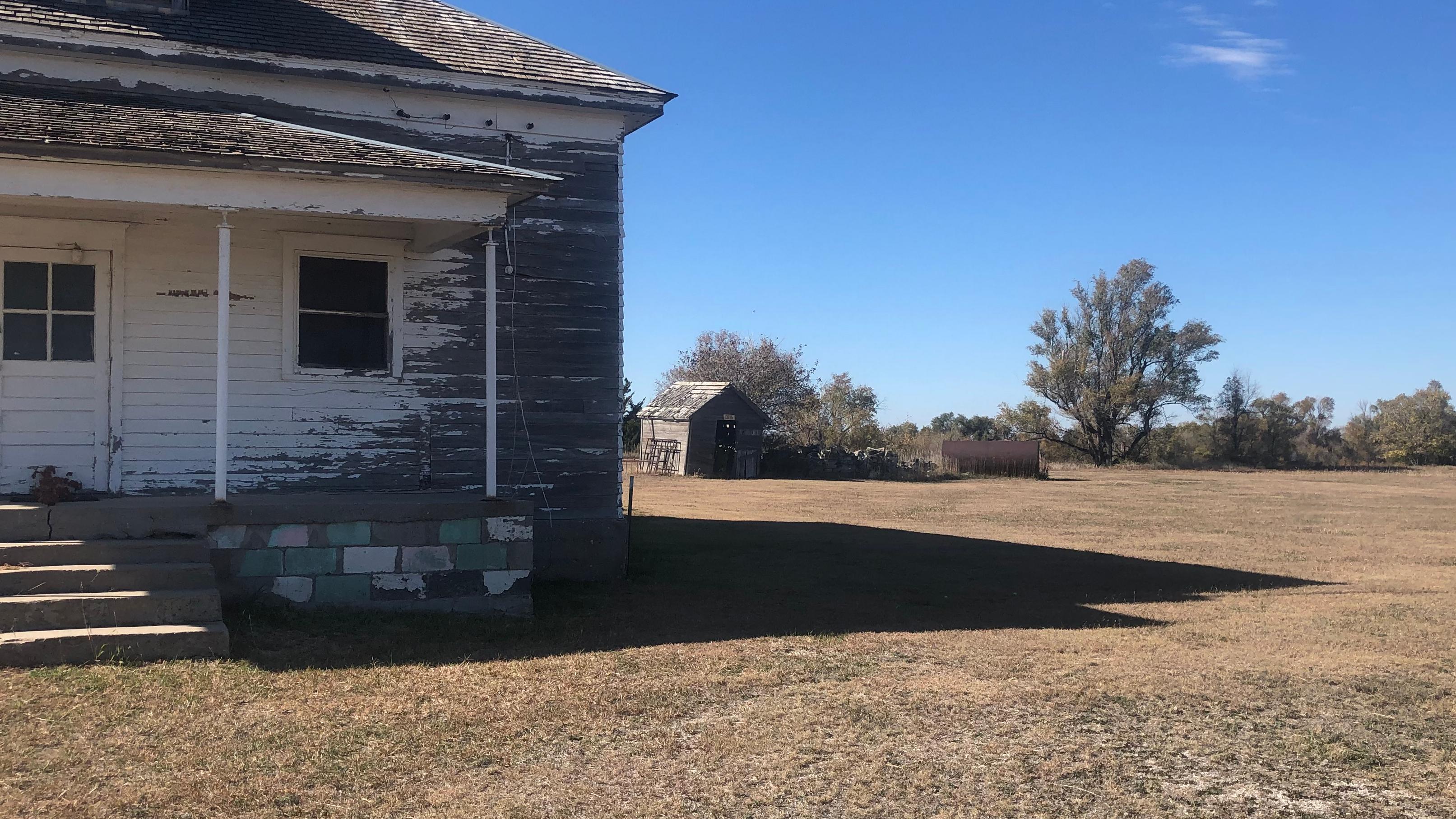 A picture of a white-painted wooden schoolhouse with trees in the background
